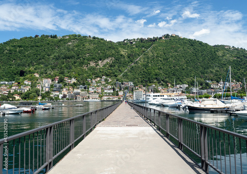 pedestrian walkway crosses the port of como, in the background the mountain with the funicular to Brunate. Lombardy, northern Italy.