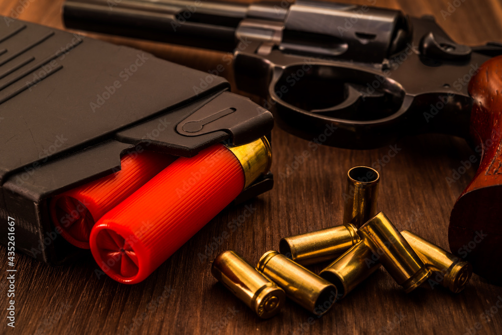 Magazines with red cartridges 12 gauge and revolver on the wooden table. Close up view Magazines with red cartridges 12 gauge and revolver on the wooden table. Close up view