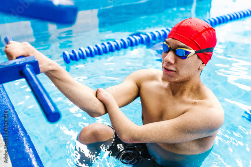 disabled latin man paralympic athlete wearing cap and goggles in a swimming training  holding On Starting Block In the Pool in disability concept with hand hypoplasia 