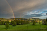 Rainbow over Bernov village in sunset evening with green meadows
