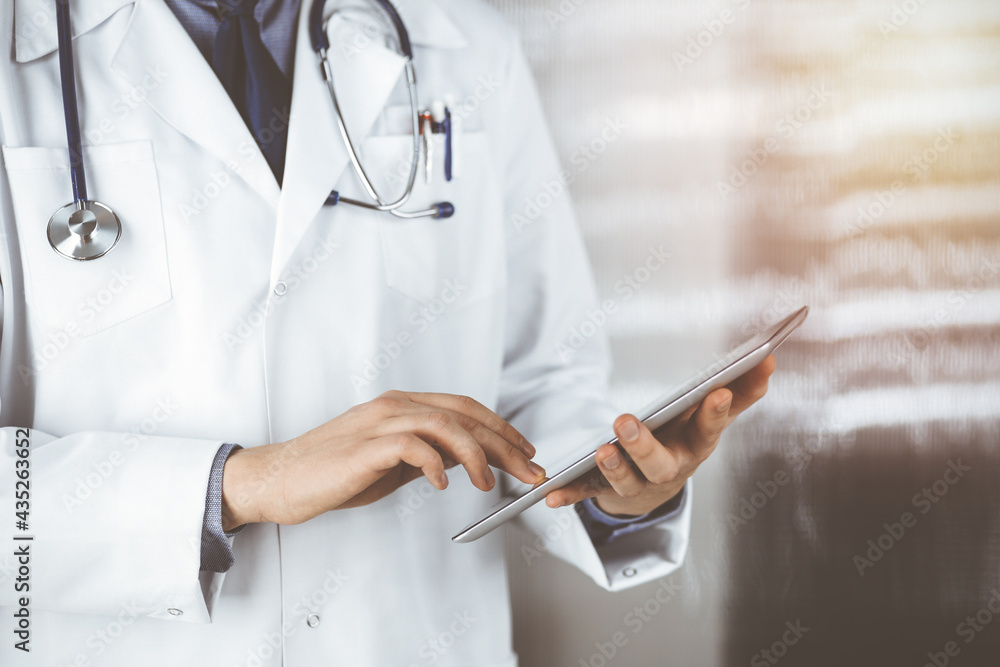 Unknown male doctor using tablet computer in sunny clinic, closeup. Perfect medical service in hospital. Medicine and healthcare concept Unknown male doctor using tablet computer in sunny clinic, closeup. Perfect medical service in hospital. Medicine and healthcare concept