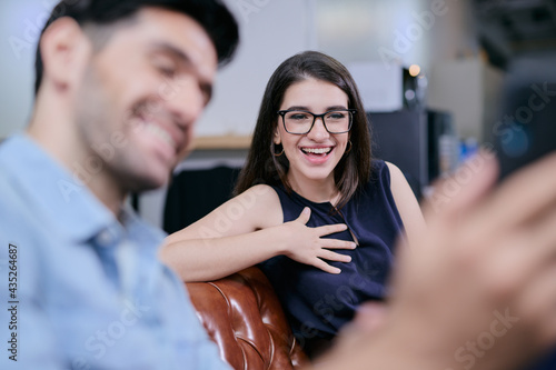 A happy businesswoman is watching something on her friend's smartphone with big smile on her face.