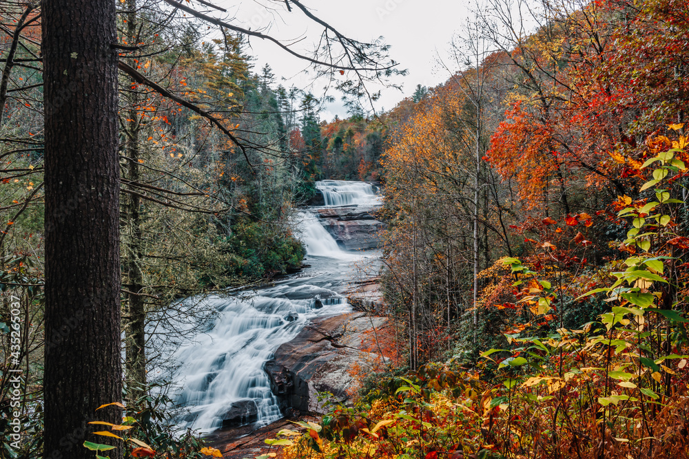 Three cascading tiers of the Triple Falls waterfall on the Little River surrounded by colorful fall foliage in DuPont State Recreational Forest, Hendersonville, North Carolina, USA. 