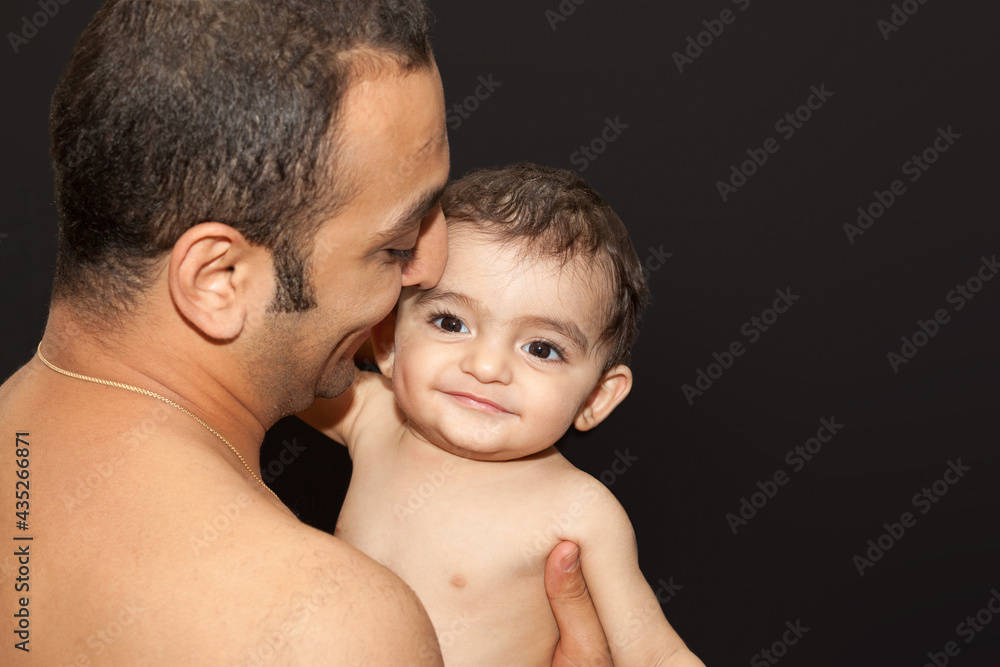 The father holds his son in his arms. Studio portrait over isolated dark background. Negative space for text The father holds his son in his arms. Studio portrait over isolated dark background. Negative space for text