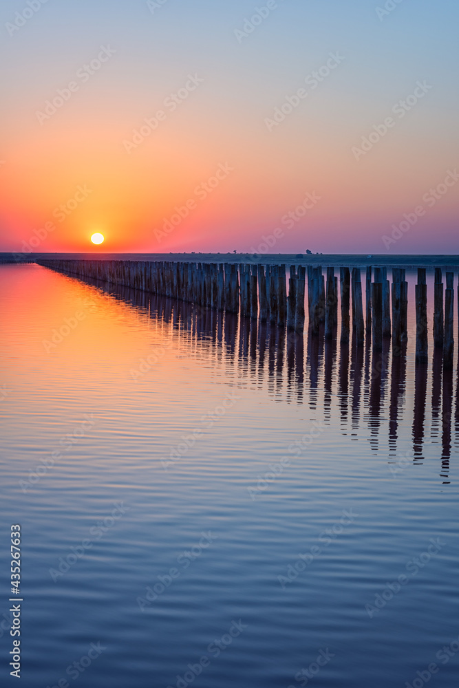 Wood posts for salt extraction in the water of extremely salty lake, amazing nature landscape in sunset light with colored sky, sun and reflection, Henichesk, Ukraine