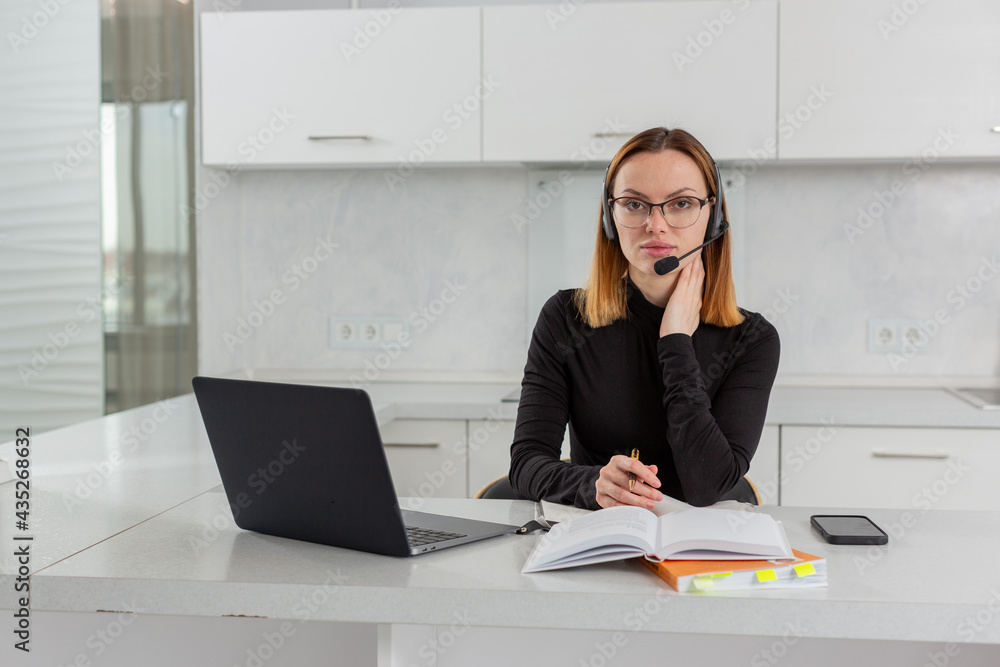 Smart girl in glasses and a headset sits at a laptop in the home office, conducts online training. High quality photo Smart girl in glasses and a headset sits at a laptop in the home office, conducts online training. High quality photo