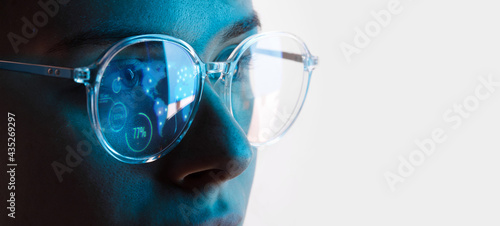 Close up view of blue eye in glasses with futuristic holographic interface to display data. Portrait of beautiful young woman, half of face. Augmented reality, future technology, internet concept. photo