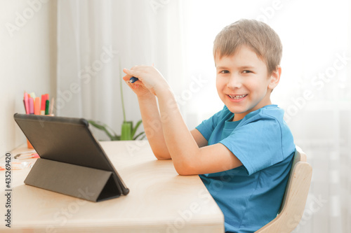 7 years old child boy doing lessons sitting at desk in his room. Happy kid learning at home using tablet. Distance education and learning concept photo