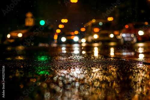 Rainy night in the big city, dense traffic at a busy avenue in the light of lanterns. View from the level of asphalt