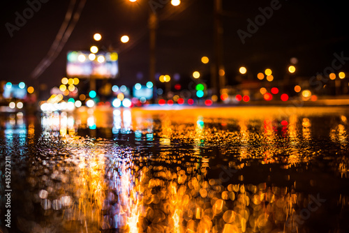 Rainy night in the big city, the light from the headlamps of approaching car on the highway. View from the level of asphalt