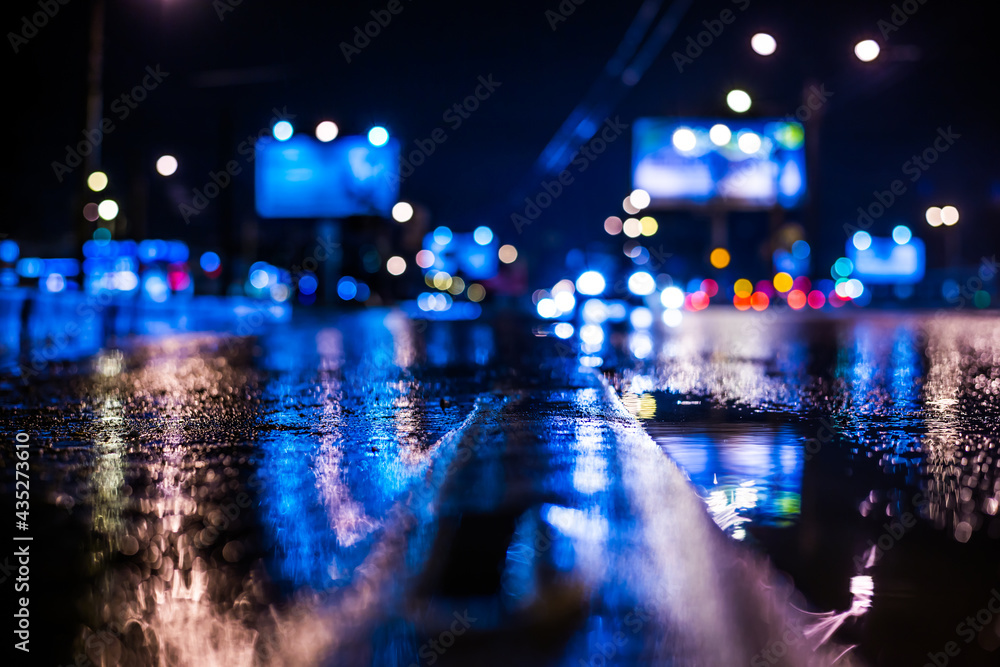 Rainy night in the big city, the light from the headlamps of approaching car on the highway. View from the level of the dividing line