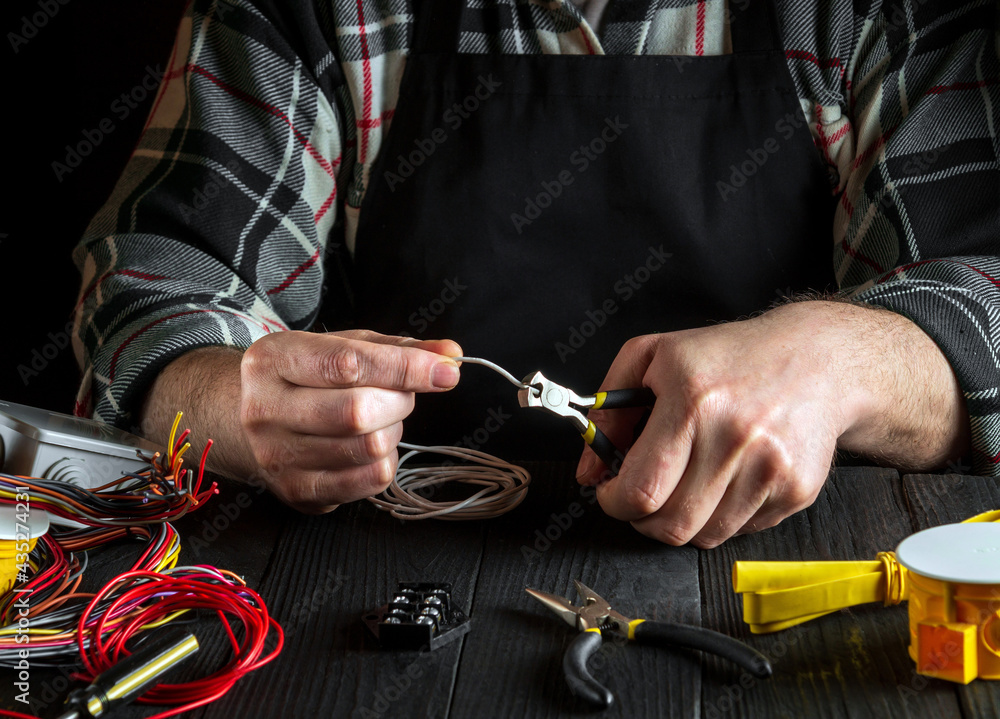 Fototapeta premium Professional master electrician cuts white wire with diagonal pliers. Working environment on the workshop table
