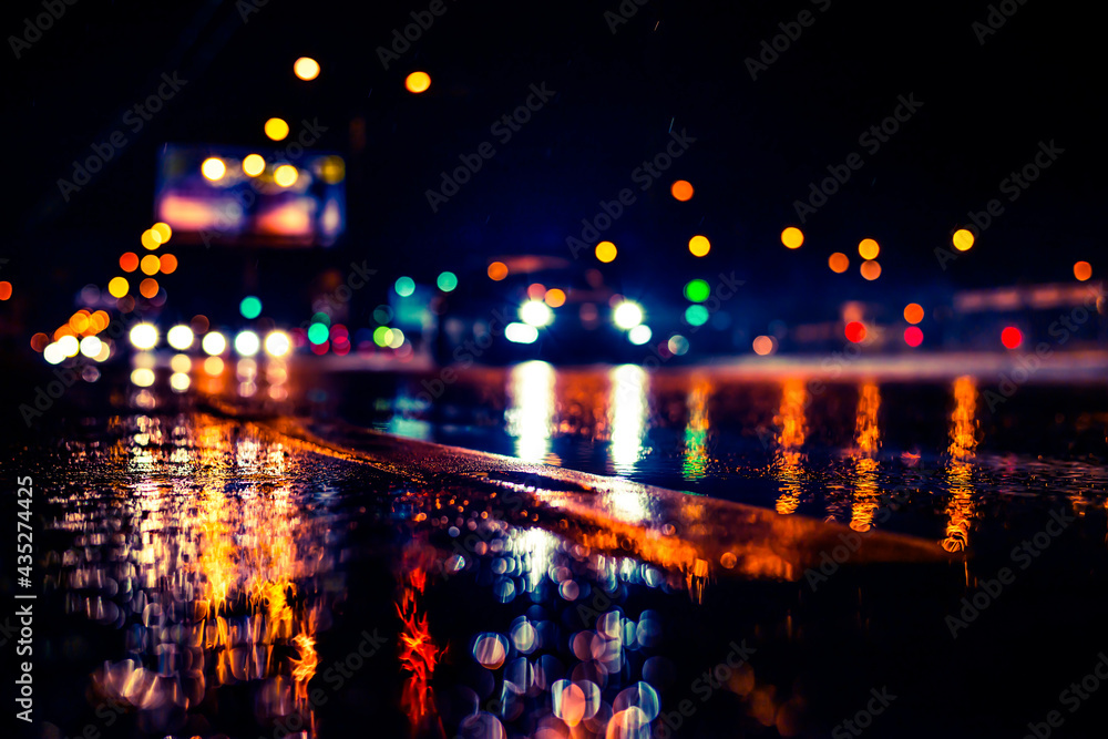 Rainy night in the big city, the light from the headlamps of approaching car on the highway. View from the level of the dividing line