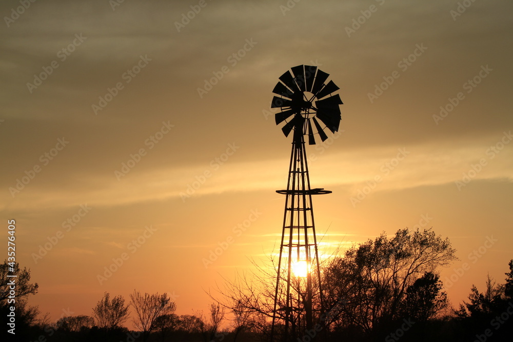 Kansas sunset with a Windmill with clouds and tree silhouette's that's bright and colorful out in the country north of Hutchinson Kansas USA.
