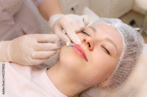 A beautiful girl is given beauty injections in the lips A master cosmetologist gives an injection to increase the lips of hyaluronic acid