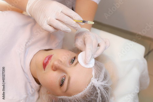 The cosmetologist holds a beauty injection syringe in front of the client's face