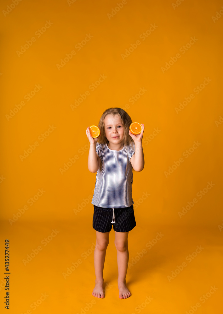 little girl stands with orange halves on a yellow background with space for text. Tropical fruits little girl stands with orange halves on a yellow background with space for text. Tropical fruits
