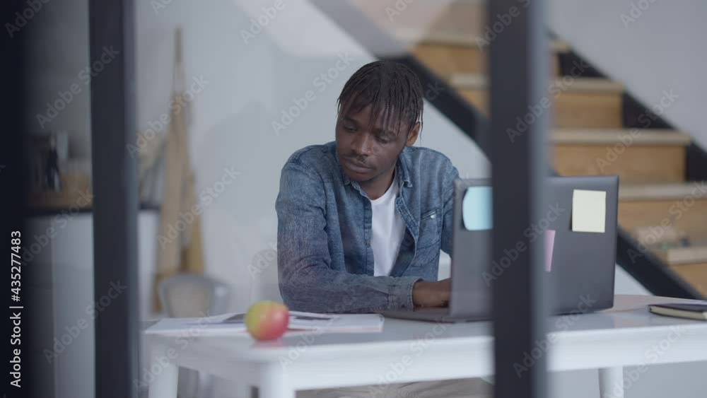 Portrait of handsome young man sitting at table typing on laptop keyboard in slow motion. Focused African American guy messaging online in home office. Lifestyle and business concept Portrait of handsome young man sitting at table typing on laptop keyboard in slow motion. Focused African American guy messaging online in home office. Lifestyle and business concept