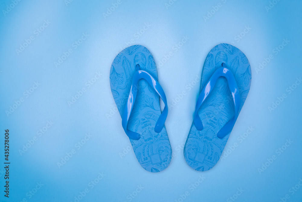 Naklejka premium Blue rubber flip-flops isolated over blue background, pair of thongs, shot above