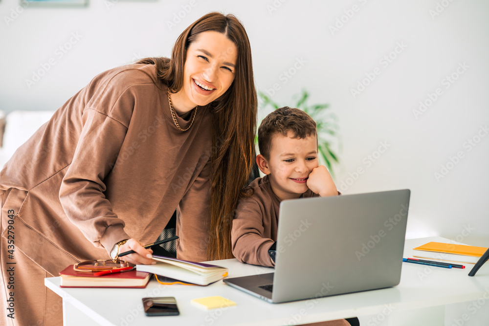 Happy mother helps her little son with online homework on laptop. Distance education Happy mother helps her little son with online homework on laptop. Distance education