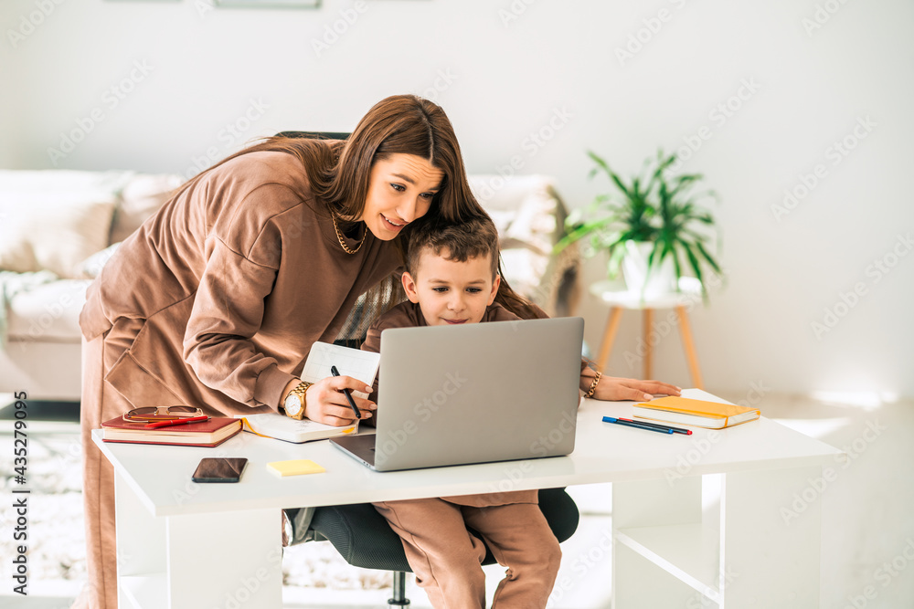 Mother helps her little son with online homework on laptop. Distance education Mother helps her little son with online homework on laptop. Distance education