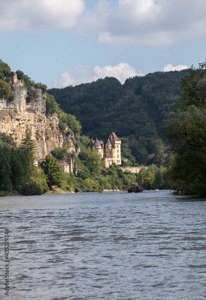 Canoeing and tourist boat, in French called gabare, on the river Dordogne at La Roque-Gageac and Chateau La Malartrie in the background. Aquitaine, France Canoeing and tourist boat, in French called gabare, on the river Dordogne at La Roque-Gageac and Chateau La Malartrie in the background. Aquitaine, France