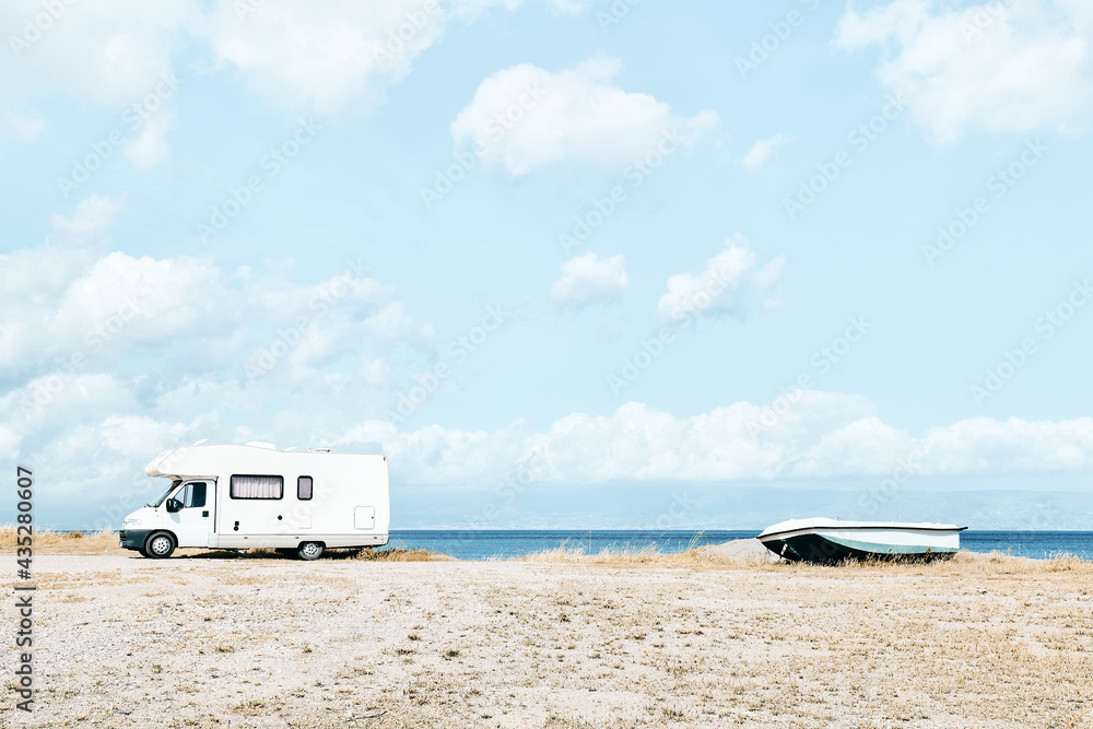 White camper van parked near the sea on the beach. Tourist season on the mediterranean sea. Sicily. Ionian sea.