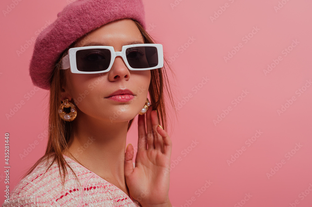Fashion close up studio portrait of elegant woman wearing classic beret, stylish rectangle white frame sunglasses, trendy pearl earrings, posing on pink background. Copy, empty space for text Fashion close up studio portrait of elegant woman wearing classic beret, stylish rectangle white frame sunglasses, trendy pearl earrings, posing on pink background. Copy, empty space for text