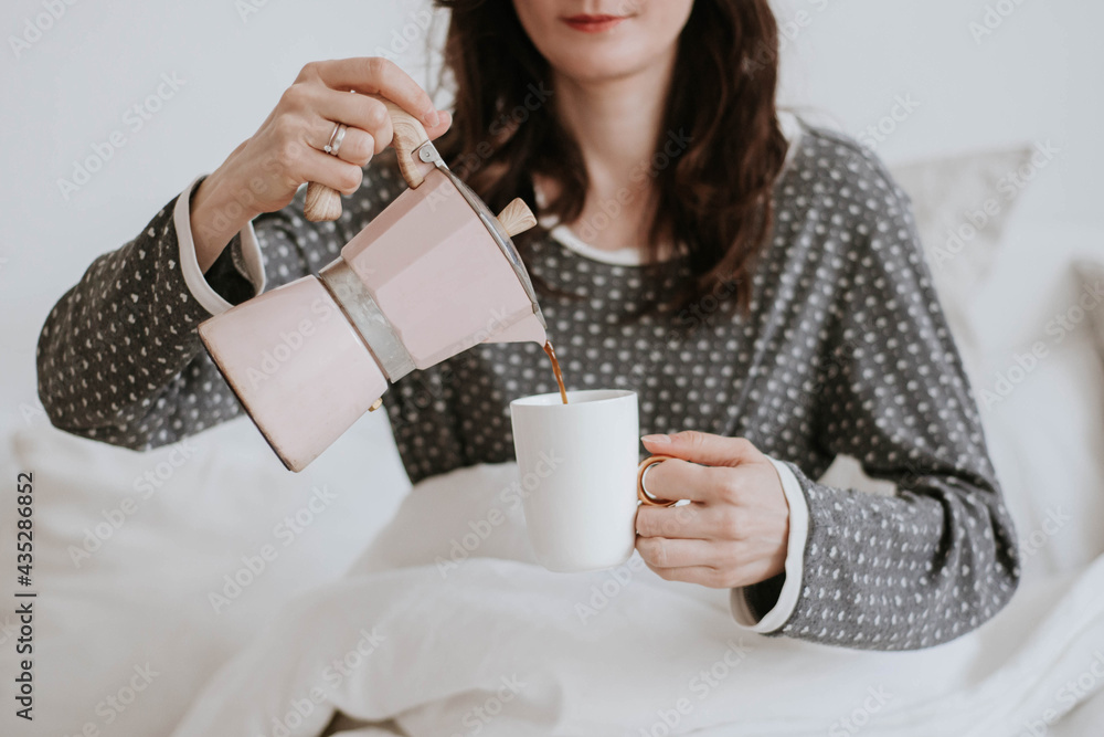 morning starts with coffee: a young woman sits on the bed and pours coffee into a cup morning starts with coffee: a young woman sits on the bed and pours coffee into a cup