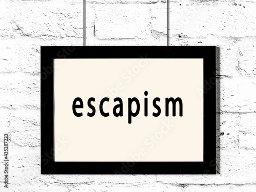 Black frame hanging on white brick wall with inscription escapism photo