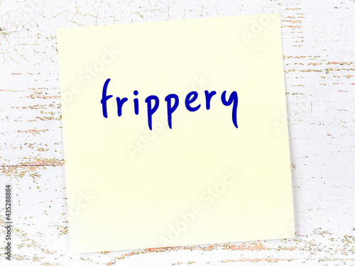 Yellow sticky note on wooden wall with handwritten word frippery