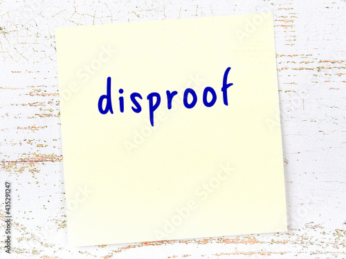 Yellow sticky note on wooden wall with handwritten word disproof photo