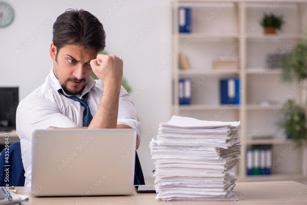 Young male employee unhappy with excessive work in the office Young male employee unhappy with excessive work in the office