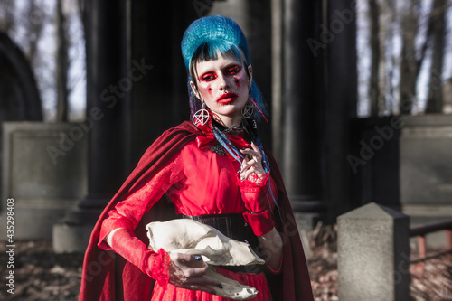 Beautiful portrait of a gothic model with an animal skull in her hands. Bright red makeup and look. Gothic-punk girl with blue hair and piercings.