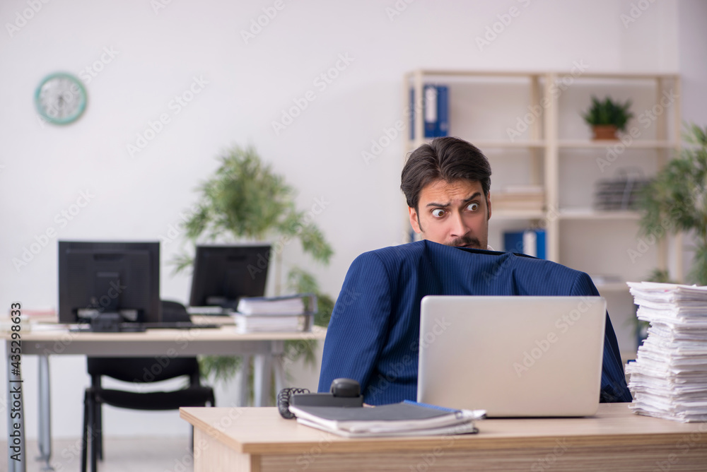 Young male employee unhappy with excessive work in the office Young male employee unhappy with excessive work in the office