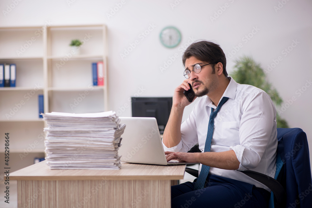 Young male employee unhappy with excessive work in the office Young male employee unhappy with excessive work in the office