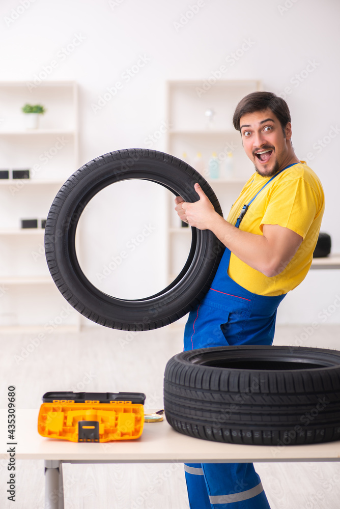 Young male garage worker with tyre at workshop Young male garage worker with tyre at workshop