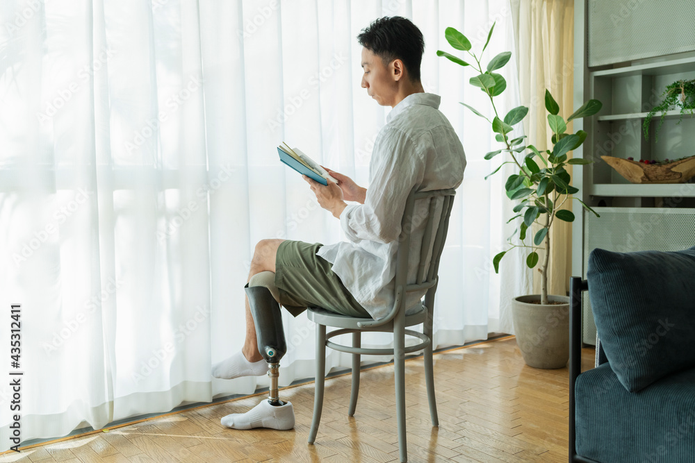 窓際で本を読む義足の男性 窓際で本を読む義足の男性