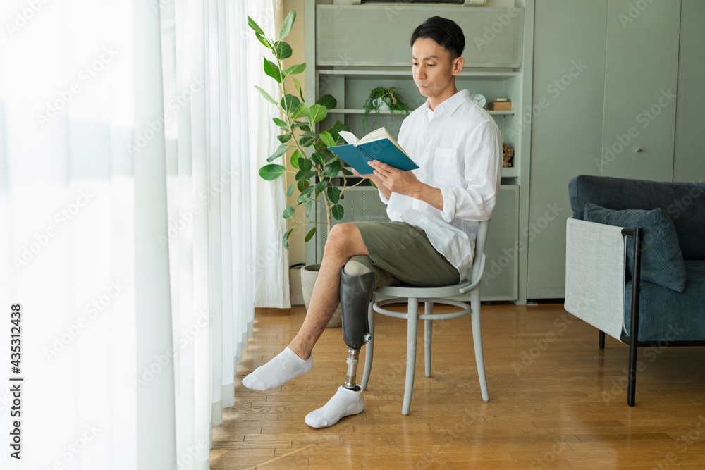 窓際で本を読む義足の男性 窓際で本を読む義足の男性
