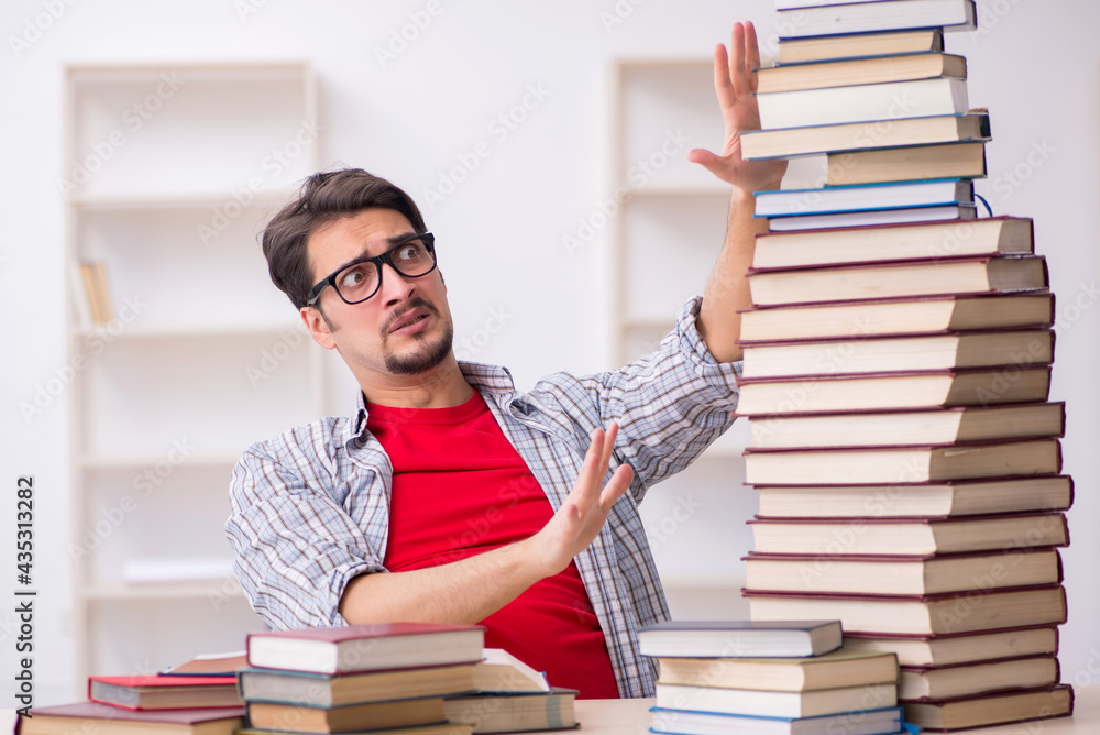Young male student and too many books in the classroom Young male student and too many books in the classroom