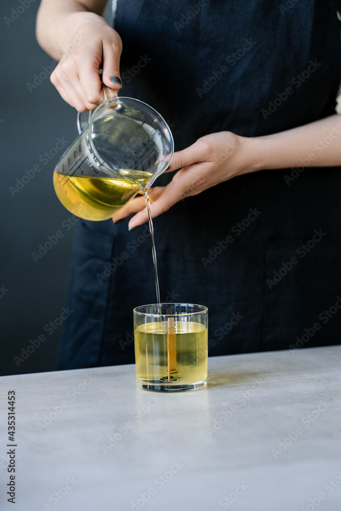 The girl pours wax into glass glasses with wicks. The girl pours wax into glass glasses with wicks.