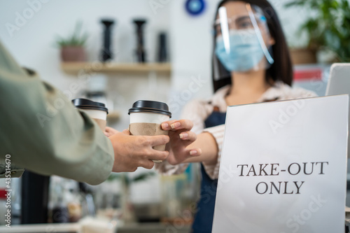 Asian waitress wearing face mask and shield serving coffee to customer