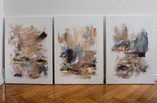 Art collection. Three contemporary abstract paintings on the wooden floor of the art studio. Nonfigurative abstract paintings of the same artistic series with colorful stains and strong brush texture 