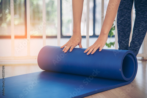 Woman hands rolled up yoga mat on gym floor in yoga fitness training room. Home workout woman close up hands rolling foam yoga gym mat. Woman barefoot home workout sportive healthy lifestyle concept