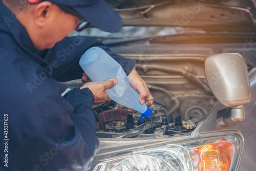 Car Mechanic man hands pouring Deionized purified Distilled water for car battery mechanical service. Close up hands man hold Deionized Distilled liquid water bottle at garage auto mobile car service photo