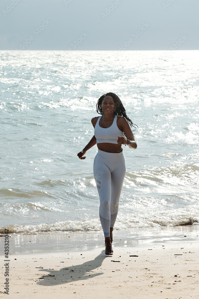 Happy fit beautiful sportswoman in activewear jogging on beach on sunny morning Happy fit beautiful sportswoman in activewear jogging on beach on sunny morning