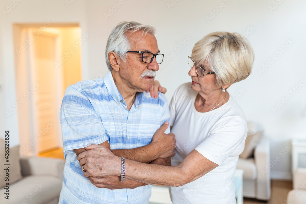 Unhappy senior man suffering from elbow pain at home. His wife taking care of him Unhappy senior man suffering from elbow pain at home. His wife taking care of him