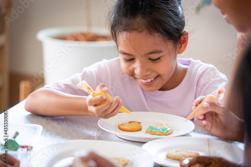 Close up asian child girl squeezing icing cream to decorate cookies with friend with fun. DIY homemade kid art and craft concept.