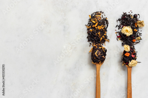 Large assortment of dry tea in spoons from herbs, flowers, berries and fruits on on stone marble countertop.