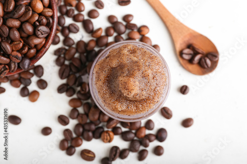 Jar with body scrub and coffee beans on light background